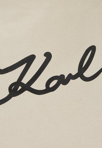 Leinenbeutel mit auffälligem schwarzen Schreibschrifttext, der "Karl" auf einem cremefarbenen Hintergrund spell. Die Textur ist glatt mit sichtbarem Stoffgewebe.