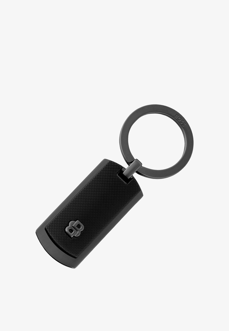 Porte-clés rectangulaire texturé noir avec un anneau métallique rond attaché, présentant un petit logo en relief sur la surface du porte-clés.