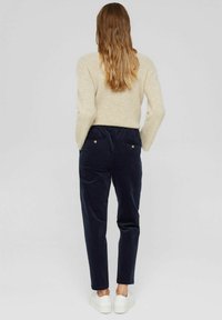 Navy-blaue Cordhosen mit lockerer Passform, ausgestattet mit einem elastischen Bund, zwei Gesäßtaschen und goldfarbenen Knöpfen, kombiniert mit weißen Sneakers.