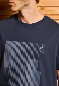 T-shirt en coton marine avec un imprimé graphique comportant des lignes verticales et des coordonnées dans des teintes plus claires. Encolure ronde et manches courtes.