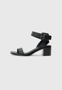 Svart lær hæl sandal med justerbar ankelstropp, åpen tå design og firkantet blokk hæl. Glatt tekstur, minimalistisk stil.