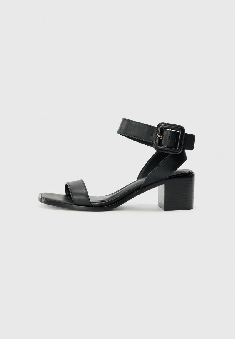 Svart lær hæl sandal med justerbar ankelstropp, åpen tå design og firkantet blokk hæl. Glatt tekstur, minimalistisk stil.