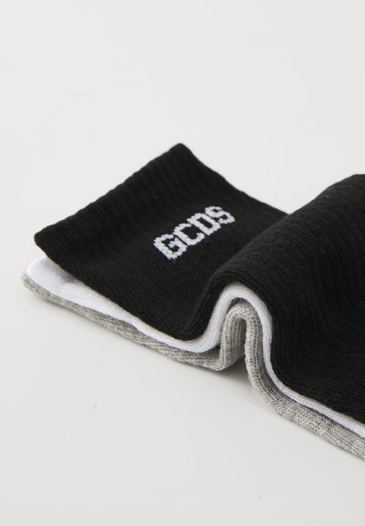 Chaussettes noires et grises avec une texture côtelée ; lettrage blanc "GCDS" sur la partie noire ; pliées à un angle pour montrer les couches et le design.