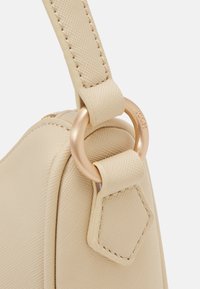 Bandoulière de sac en cuir beige texturé attachée à un anneau en métal doré gravé du nom de la marque Joop.