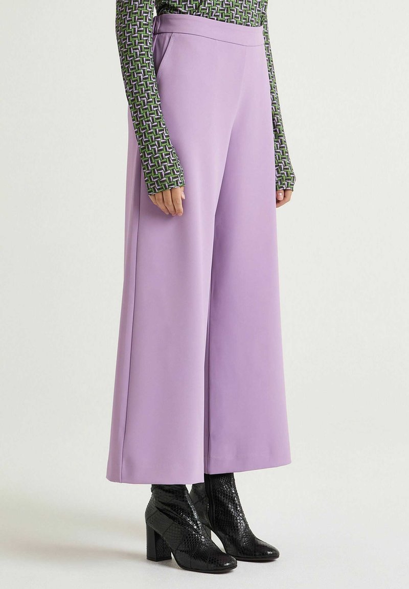Wide-legged, lavender trousers made of smooth fabric, featuring a high waist and paired with black, textured ankle boots.
