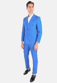 Completo blu brillante a doppio petto con finitura testurizzata, dotato di bottoni viola. Abbinato a mocassini neri per un look completo.