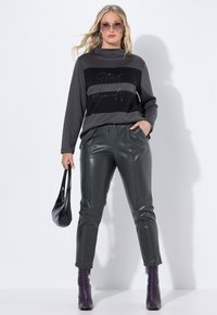 Černé a šedé tričko s dlouhým rukávem a třpytivým textem, spárované s tmavě zelenými kalhotami z umělé kůže a fialovými kotníkovými botami. Součástí je černá taška.