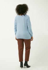 Hellblauer Pullover mit Rundhalsausschnitt, geripptem Saum und langen Ärmeln, kombiniert mit braunen tapered Hosen und schwarzen, hohen Stiefeletten.