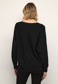 Fekete, oversized pulóver széles nyakkivágással, bordás mandzsettával és szegéllyel. Puha anyag, sima tapintással. Hátulnézet, amelyen az eső vállak látszanak.