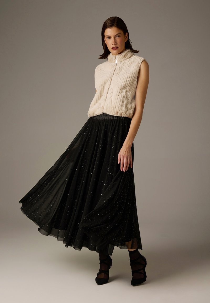 Ärmellose Weste in Creme mit strukturiertem Stoff, kombiniert mit einem fließenden schwarzen Rock, der mit schimmernden silbernen Punkten für zusätzliche Details verziert ist.