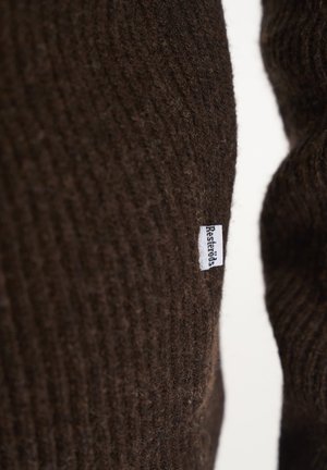 Brun strikket sweaterstof med ribbet struktur. Har et lille hvidt mærke med "Restros" på siden. Nærbillede.