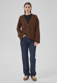Brown wool cardigan with a v-neck, four buttons, and ribbed cuffs, paired with dark blue straight-leg jeans and brown sneakers.