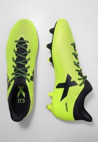 Jasně neonově žluté fotbalové boty s horní částí z síťoviny, černými akcenty, trojúhelníkovými klepacími špunty a logem X. Texturované pro lepší úchop a výkon.
