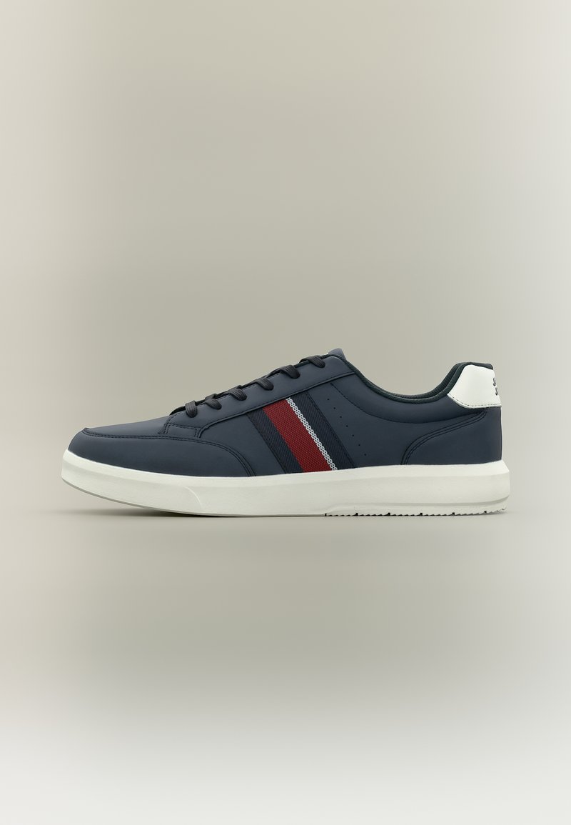 Κάλτσα αθλητικού παπουτσιού σε σκούρο μπλε χρώμα με λευκή σόλα, κόκκινες και ναυτικές ρίγες στο πλάι, μαύρα κορδόνια και λευκή ταμπέλα στη φτέρνα.