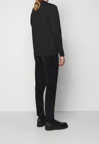 Felpa nera con collo tondo e polsini a costine, abbinata a pantaloni in velluto a coste neri. Scarpe nere mocassini con superficie liscia.