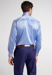 Camicia azzurra chiara a maniche lunghe con una texture liscia, colletto a contrasto e polsini abbottonati, abbinata a pantaloni blu scuro e una cintura marrone.
