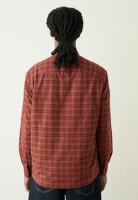 Pikad varrukad särk punase ja musta ruudulise mustriga, millel on nööpidega krae ja nööpidega mansetid, valmistatud tekstuurilisest kangast.