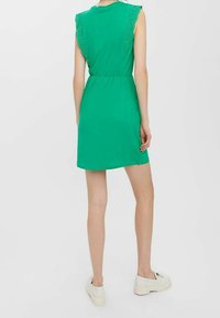 Zelené šaty s krátkými rukávy, s krajkovým lemem na ramenech. Elastický pás a délka po kolena. Nosené s bílými teniskami.