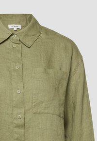 Chemise en lin vert olive clair avec boutonnage frontal, poche poitrine et col classique.