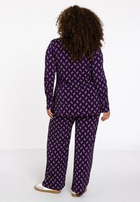 Lila gemustertes Loungewear-Set mit floralen Motiven. Langärmliges Oberteil und weite Hose, aus weichem, strukturiertem Stoff. Lässiges Design.