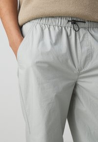 Light gray, lightweight pants with an elastic waistband and drawstring. Features side pockets and a smooth, slightly wrinkled texture.