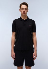 Svart polo skjorte i bomullsblanding, med krage, kortermet, og en liten logo på brystet. Brukt sammen med matchende svarte shorts.