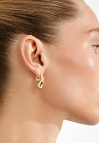 Kuldmetallist kõrvarõngad, millel on voolujooneline laineline disain. Detailidel on läikiv pind ja väike sfääriline aktsent, mis rõhutab nende elegantsi.