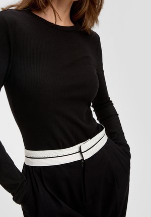 Schwarzes geripptes Langarmoberteil kombiniert mit hochgeschnittenen schwarzen Hosen, akzentuiert durch einen weißen Gürtel mit schwarzer Naht. Glatte Textur und enganliegendes Design.