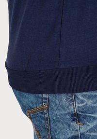 Marineblauw katoenen T-shirt met een ribbelrand, gecombineerd met lichtblauwe spijkerbroek met contrasterende gele stiksels en zakdetails.