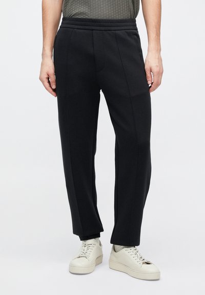 Juodi laisvo kirpimo sportiniai kelnės, turinčios ribbint juosmenį ir dvi priekines siūlių detales. Derintos su smėlio spalvos sportbačiais.