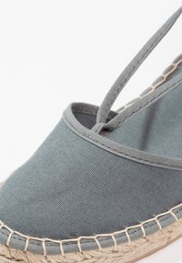 Šedé plátěné espadrilky s pletenou jutovou podrážkou, kulatou špičkou a štíhlými pásky. Prošívání podél okraje.