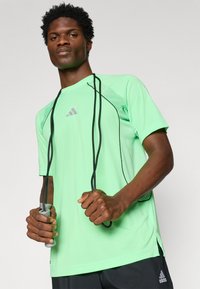 Light green athletic shirt with a round neckline, short sleeves, and subtle mesh detailing. Black accents and a gray logo on the chest.