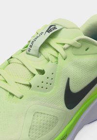 Κοντινό πλάνο ενός νέον πράσινου παπουτσιού για τρέξιμο Nike με υλικό από δίχτυ, μαύρο λογότυπο swoosh και ετικέτα "RUN Structure 26" στη γλώσσα.