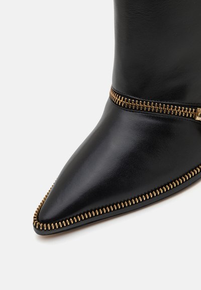 Zwarte leren enkelboot met een spitse neus, voorzien van gouden ritsdetails langs de rand. Gladde textuur en strak ontwerp.