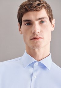 Camicia azzurro chiaro con colletto alla francese, texture liscia e due bottoni visibili al collo. Design semplice senza motivi.
