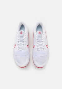 Paire de chaussures de sport blanches avec des accents rouges, tige en mesh, lacets et bande velcro, vues de dessus sur un fond uni.