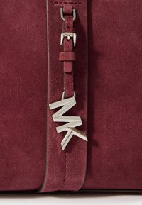 Bordo suđena torbica s detaljom od srebrnog toniranog hardvera s slovima "MK" i elegantnim, glatkim dizajnom.