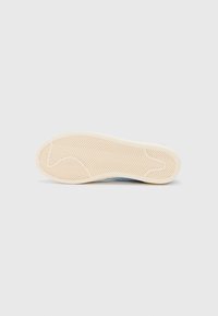 Semelle de sneaker blanche avec un motif en chevrons, présentant une base en caoutchouc crème et des accents bleu clair sur le bord supérieur.
