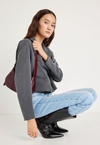 Szürke, rövidített blézer, világoskék farmer és fekete, hegyes orrú csizma. Bordó, texturált részletekkel díszített táska, vállra vetve.