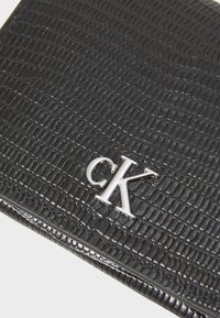 Crni teksturirani kožni novčanik s uzorkom croco kože koji se ističe, a u donjem desnom kutu nalazi se srebrni logo "CK".