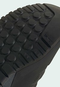 Schwarze Gummisohlen eines Schuhs mit kreisförmigen Profilmustern, glatter Oberfläche und strukturierten Kanten für besseren Halt und Stabilität. Mit "5.10." gekennzeichnet.