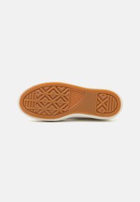 Suela de zapatilla de goma con un patrón texturizado y geométrico; presenta un borde superior de color claro y una parte inferior marrón para mayor tracción.
