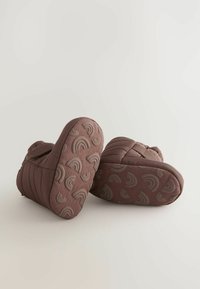 Braune gepolsterte Stiefel mit gerippter Textur, die geschwungene regenbogenförmige Muster auf der Gummisohle aufweisen. Verstellbarer Riemen für eine gute Passform.