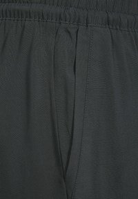 Ciemnoszara tkanina o miękkiej teksturze; posiada elastyczny pas i przeszycia wzdłuż boków, co zapewnia luźny krój.