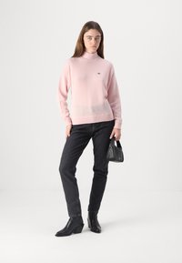Mjukt rosa polotröja med avslappnad passform, tillverkad av textilmaterial. Kombinerad med svarta jeans och svarta klackankor.
