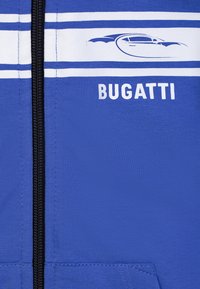 Garment blu con zip caratterizzato da strisce orizzontali bianche e la scritta "BUGATTI" stampata in bianco. Tessuto morbido e liscio con un design aderente.