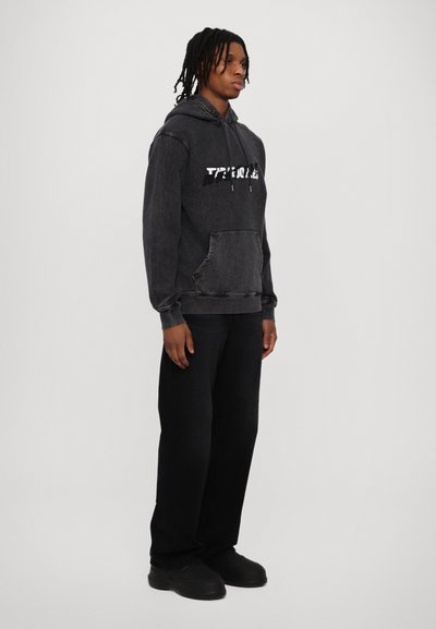 Black hoodie with a front pocket and white graphic text, paired with black jeans and black shoes. The fabric appears soft and slightly faded.