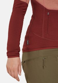 Camiseta de manga larga de canalé en burdeos con un diseño sin costuras, que cuenta con un bolsillo lateral y un corte ajustado, combinada con pantalones verdes texturizados.