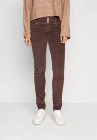 Hnědé kordové skinny džíny s vysokým pasem, které mají tři knoflíky, dvě přední kapsy a strukturovanou tkaninu.
