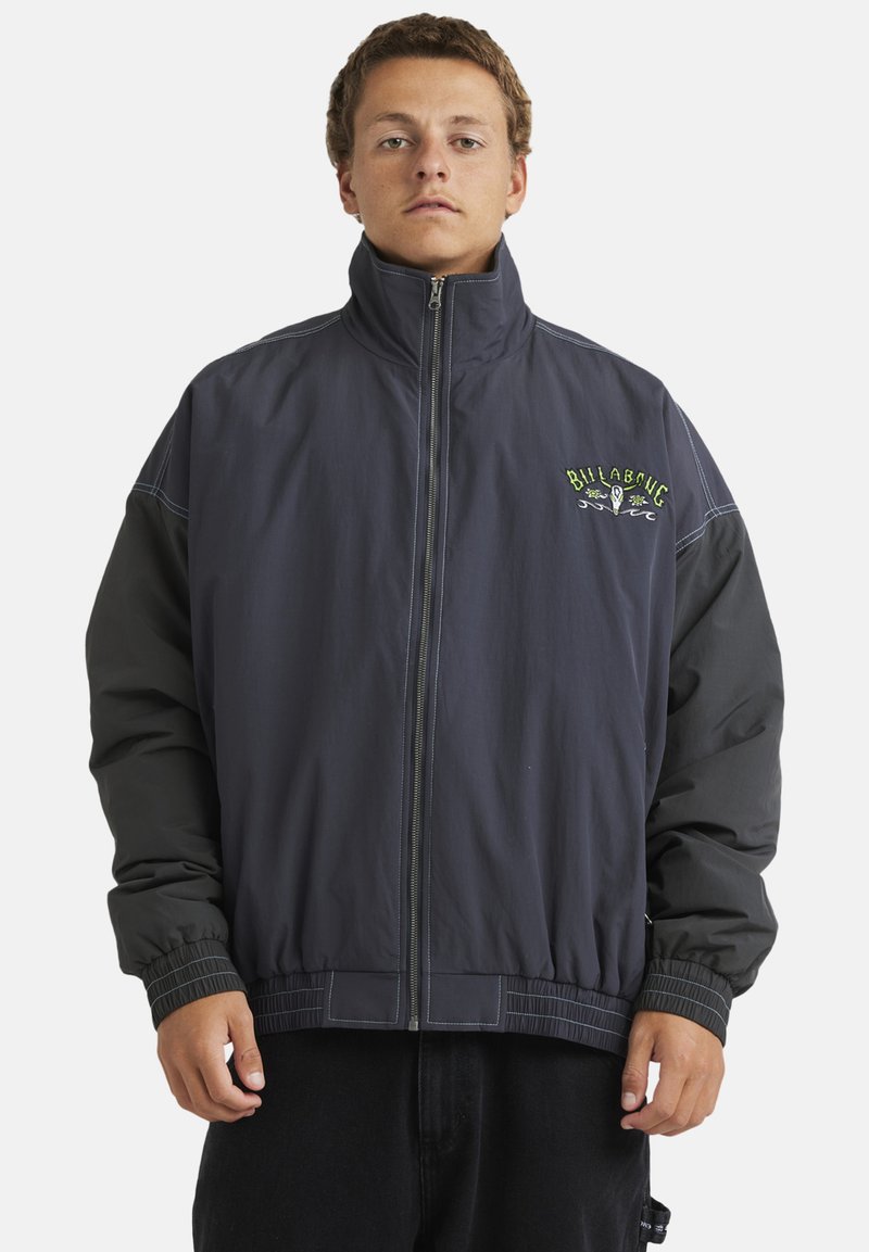 Dark gray and black jacket with high collar, elastic cuffs, and hem. Features green embroidered logo on the chest and contrasting stitching.